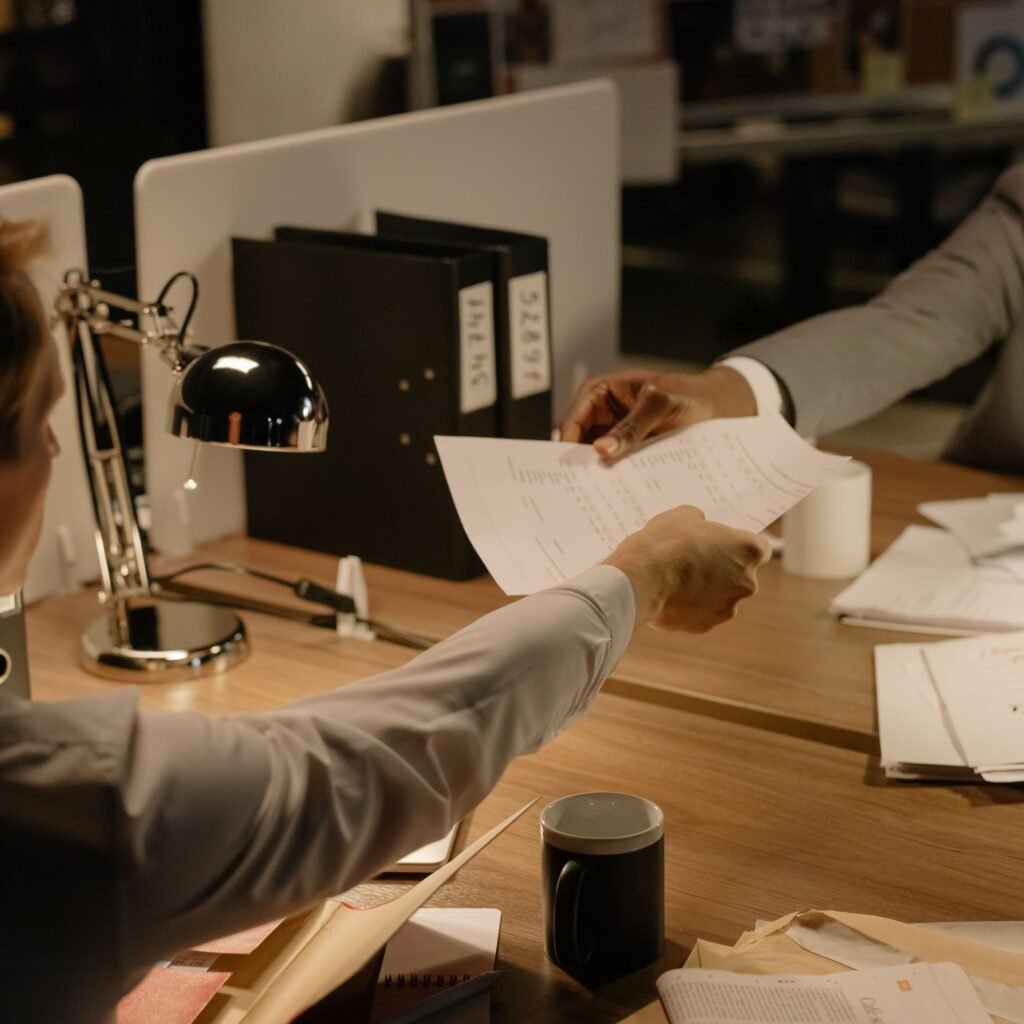 Two business professionals exchanging documents in a collaborative office setting.