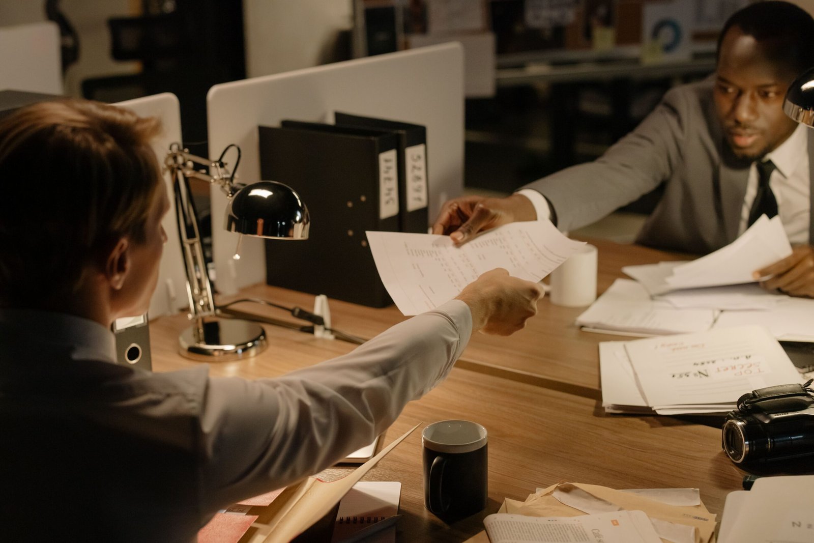 Two business professionals exchanging documents in a collaborative office setting.