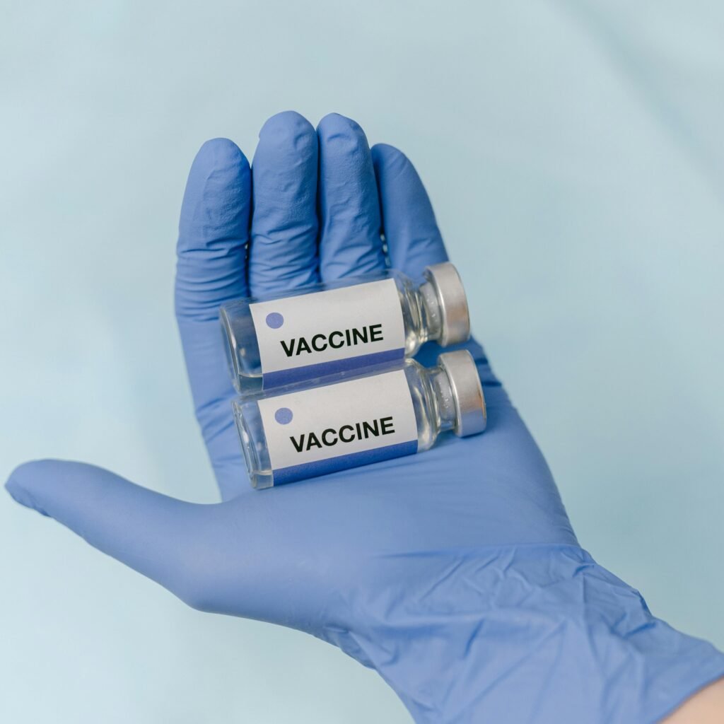 Two vaccine vials held securely in a latex-gloved hand, against a neutral background.