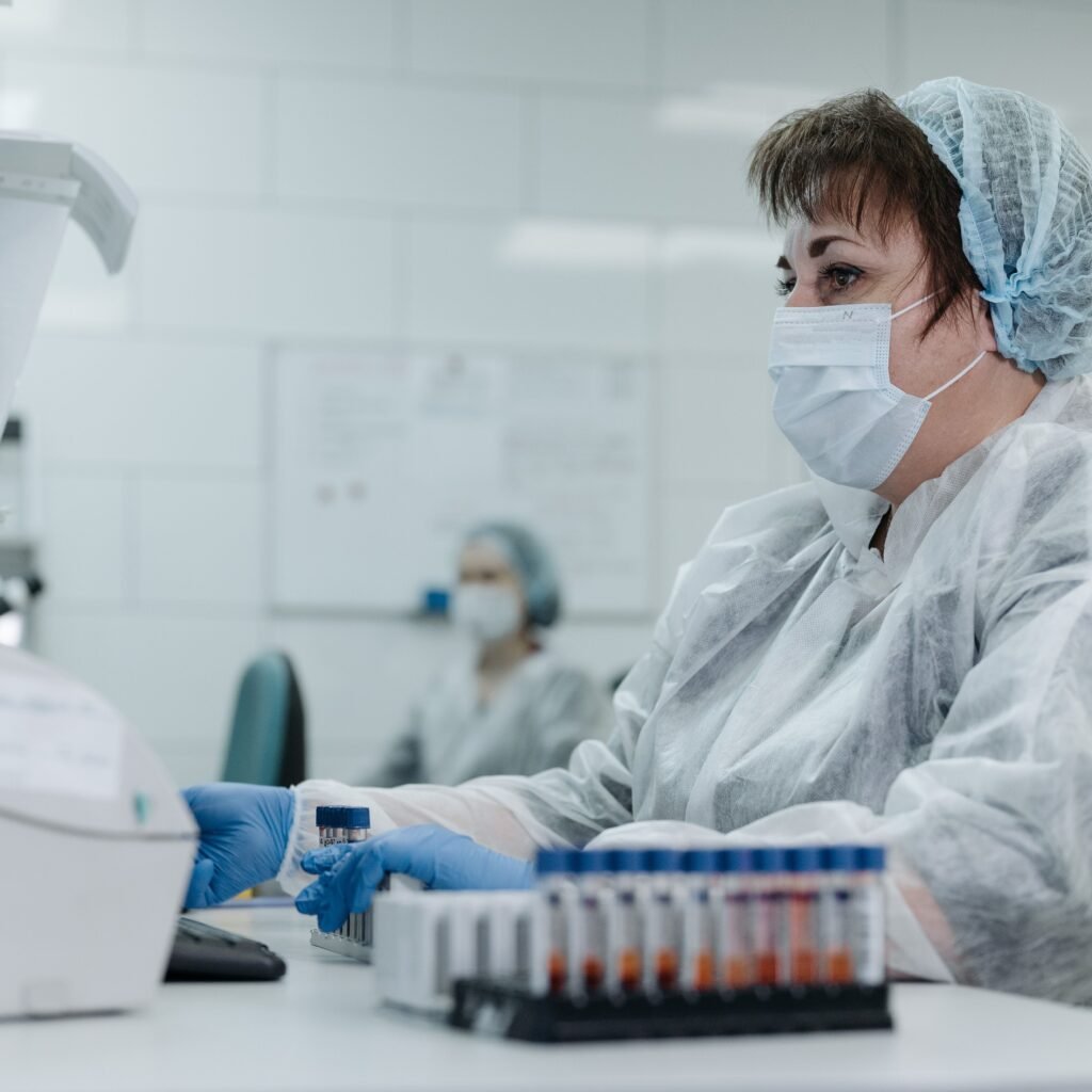 Scientist in protective gear working with lab equipment and samples in a laboratory setting.