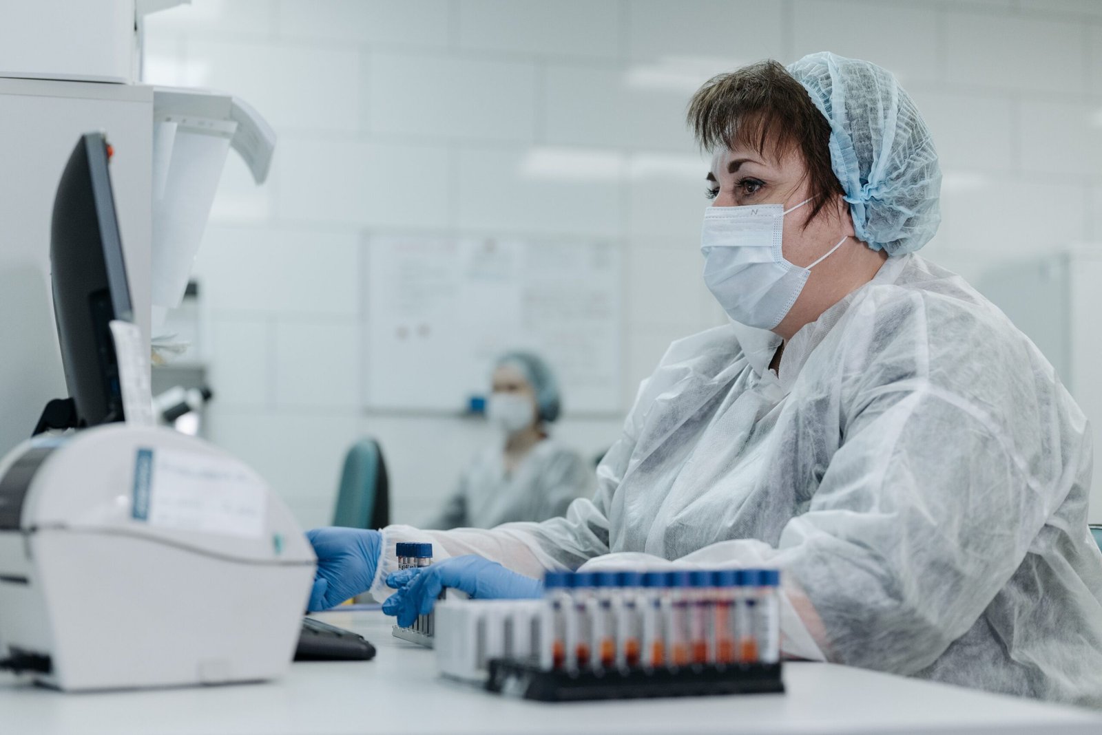 Scientist in protective gear working with lab equipment and samples in a laboratory setting.