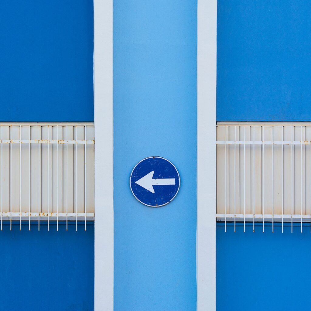 A blue wall exterior with a left-pointing arrow sign and metal railings.