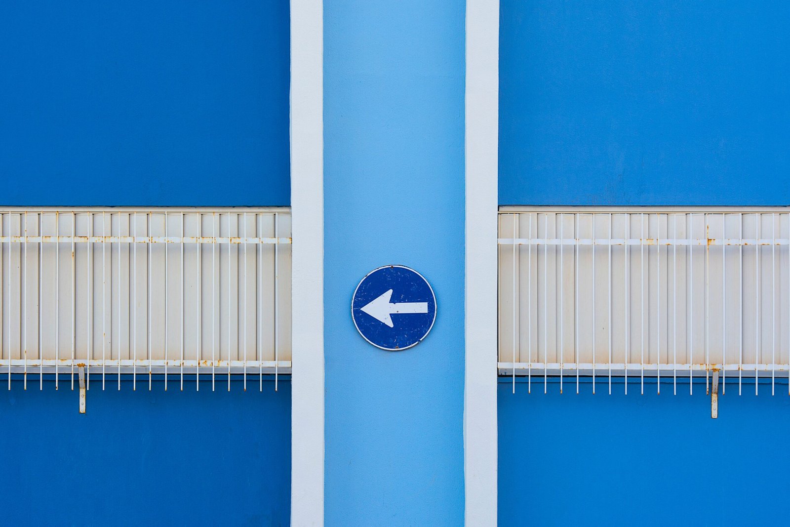 A blue wall exterior with a left-pointing arrow sign and metal railings.