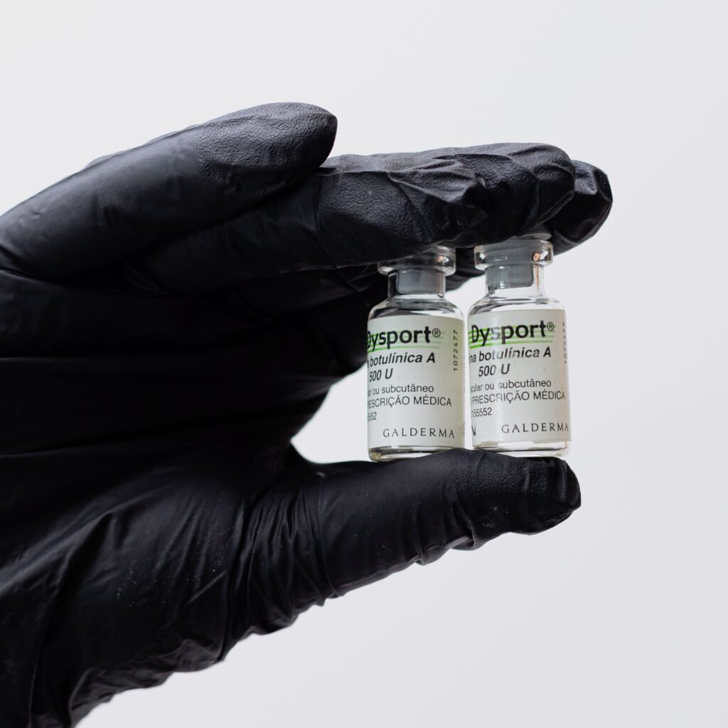 Close-up of black gloved hand holding two Botox vials in a medical setting.