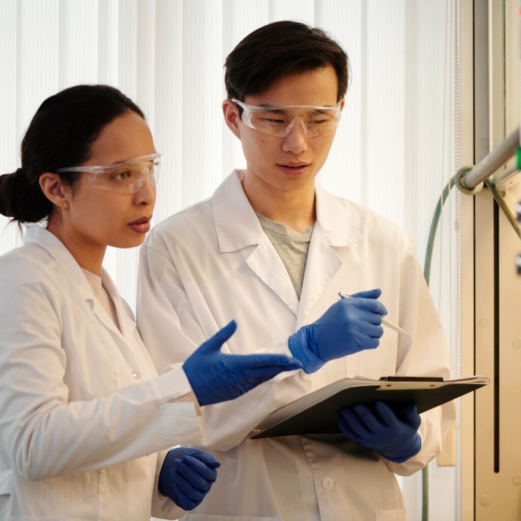 Researchers discussing data in a laboratory setting, wearing safety gear and blue gloves.