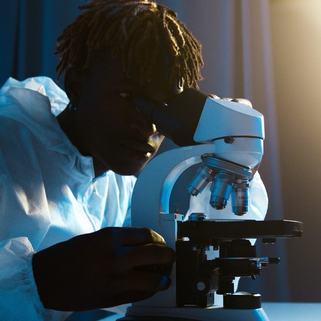 A scientist in protective clothing uses a microscope for research in a laboratory setting.