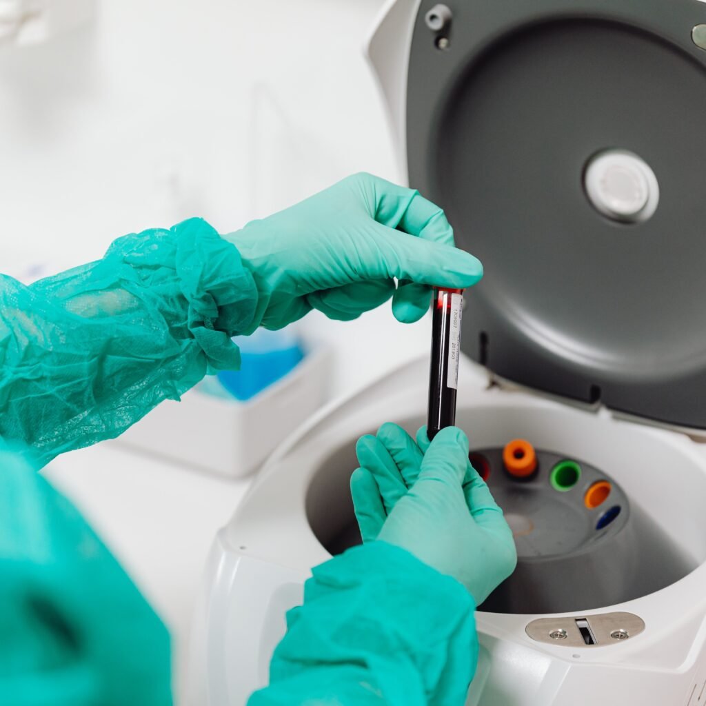 Lab technician operates a centrifuge machine, handling tubes with gloves.