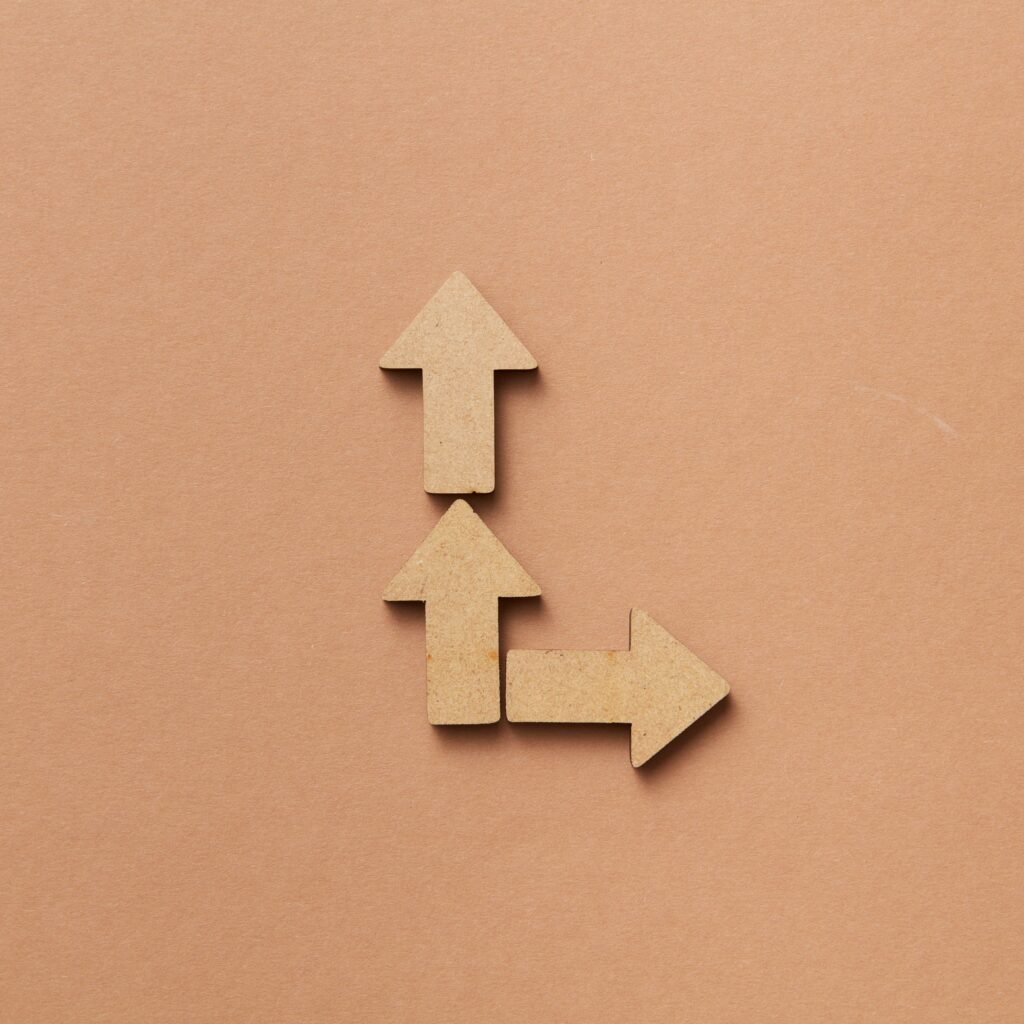 Three cardboard arrows arranged on a brown background, symbolizing direction and choice.
