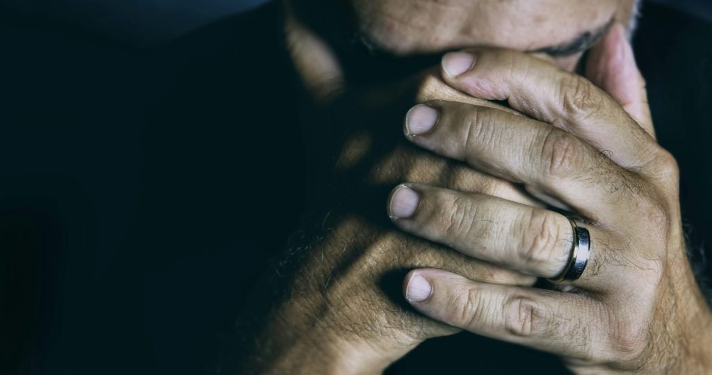 Close-up of an elderly man covering his face, expressing sadness and contemplation.