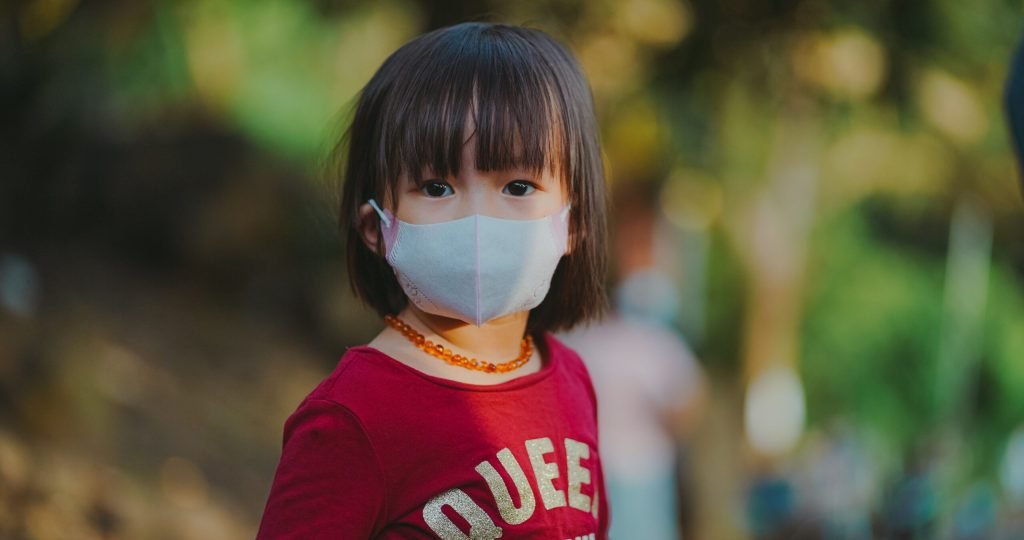 Adorable young girl wearing a face mask outdoors, emphasizing protection during pandemic.