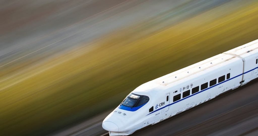 A sleek white high-speed train traveling at top speed, captured with a motion blur effect.