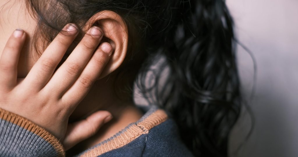 A young girl with long dark hair covering her ear in a thoughtful pose.