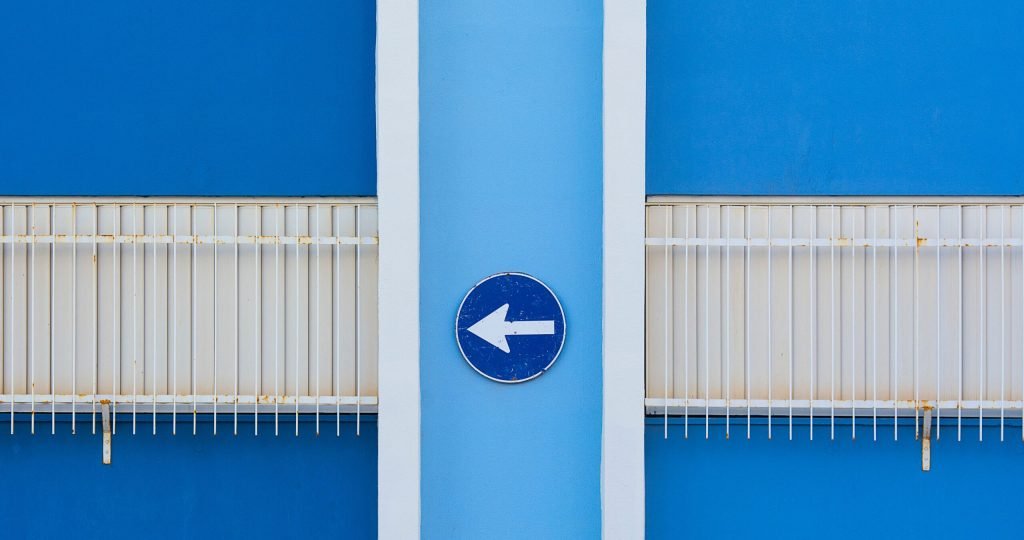 A blue wall exterior with a left-pointing arrow sign and metal railings.
