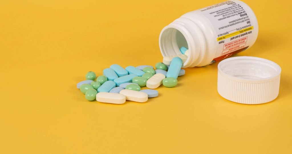 Various pills spill from a bottle onto a vibrant yellow surface, highlighting health themes.