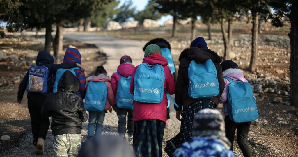 A group of children with UNICEF backpacks walking on a dirt road in rural Syria.