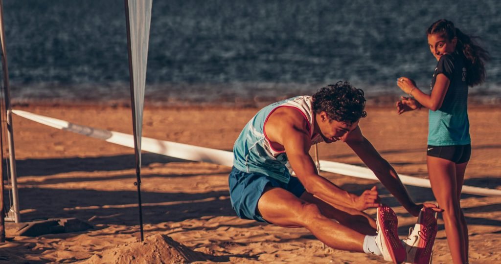 Athletes perform long jump on the beach in Sada, Spain, capturing energetic action in the sun.