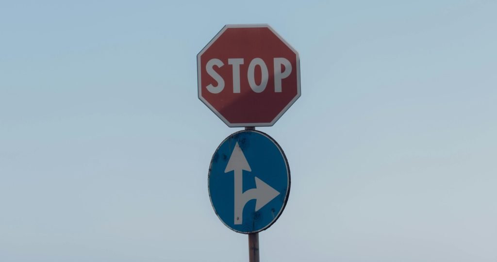 Stop sign with directional arrows at Lido di Noto, Sicily with sky backdrop.