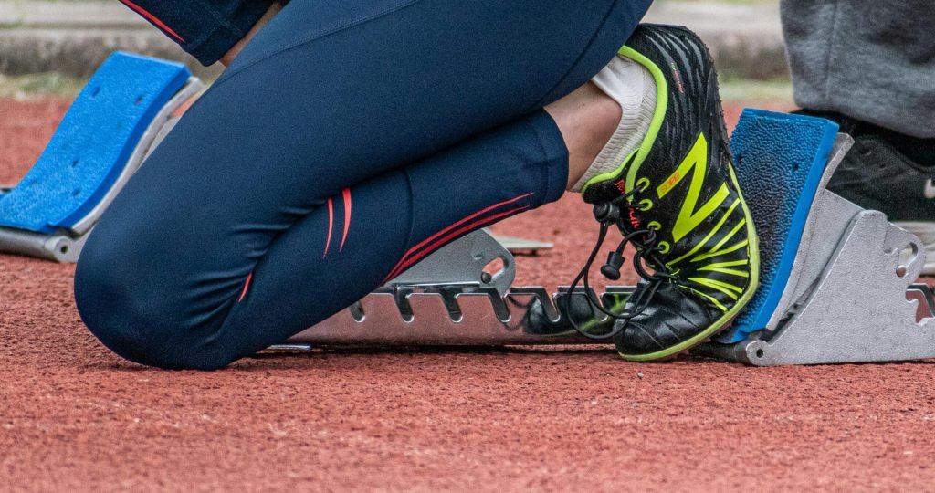 Close-up of a runner's legs ready to start a race, showcasing running shoes and starting block.