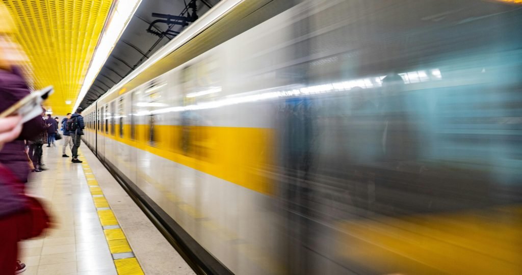 Blurred motion of a train speeding through a vibrant subway platform with commuters.