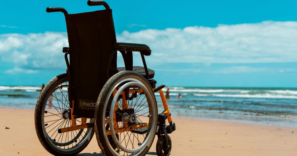 A wheelchair on a sandy beach overlooking the sea on a bright summer day.