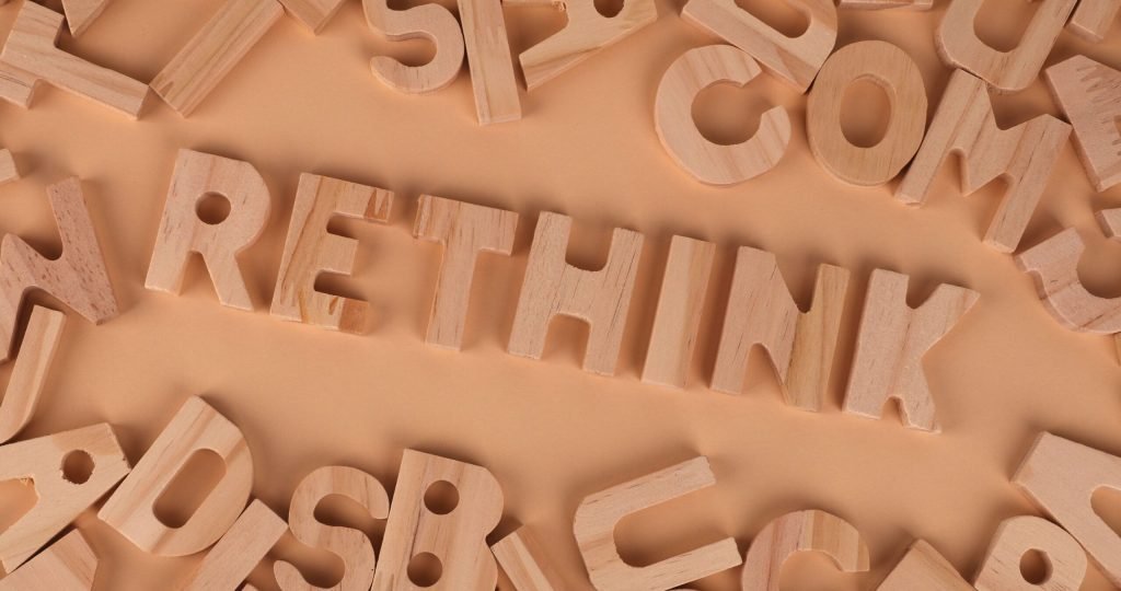 Wooden alphabet letters forming the word rethink on a flat, peach-colored background.