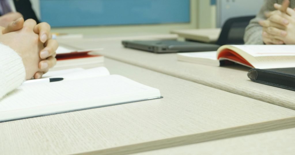 Close-up of a professional meeting setup with hands, laptops, and notebooks on a wooden desk.