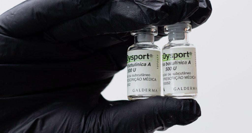 Close-up of black gloved hand holding two Botox vials in a medical setting.