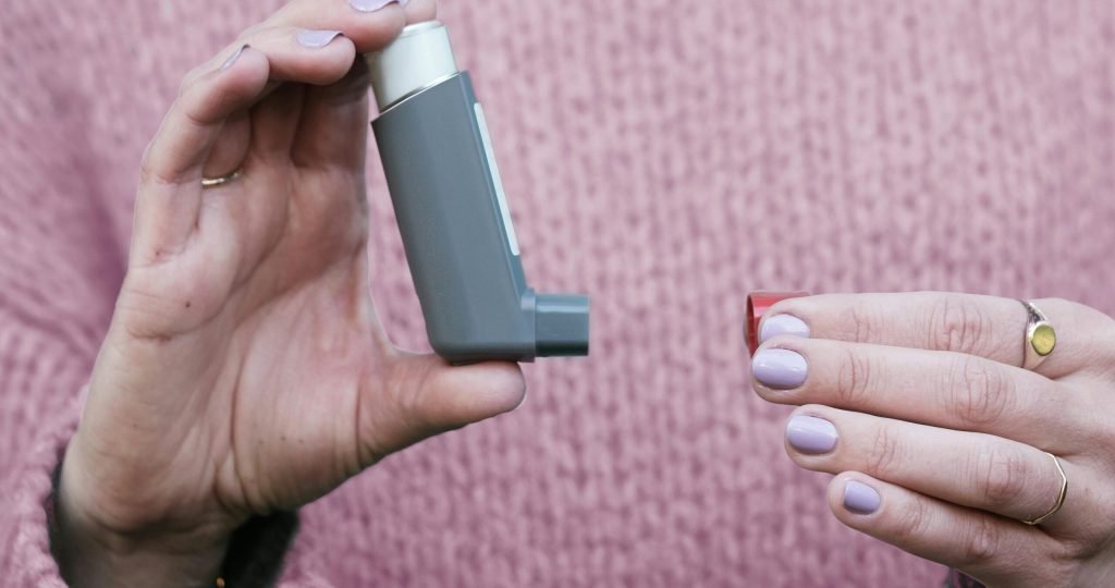 Woman holding a gray inhaler against a pink sweater. Essential asthma medication concept.