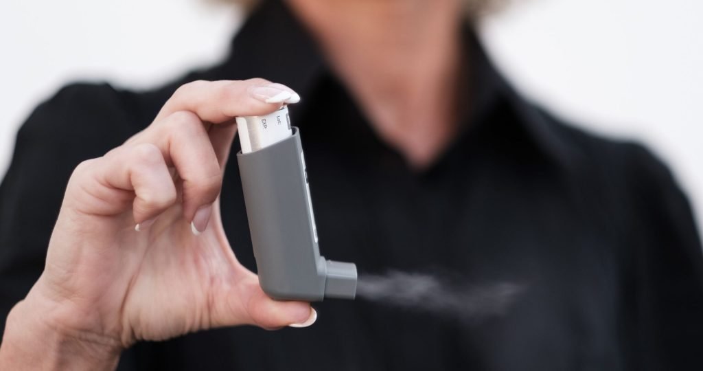Person holding and using an inhaler, showcasing healthcare and respiratory care indoors.