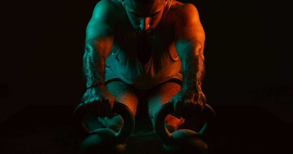 A strong man intensely working out with kettlebells in a dark gym setting.