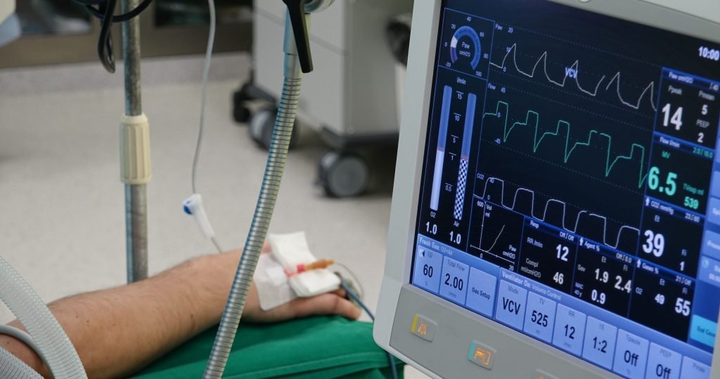 A close-up of a patient's hand connected to medical equipment in an ICU room.