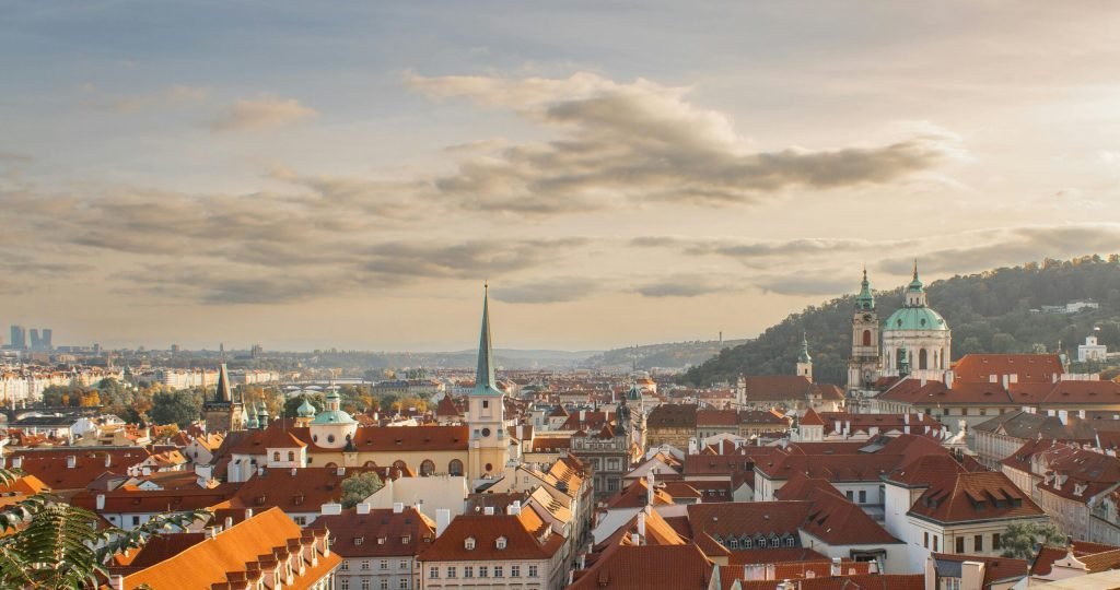 Captivating view of Prague's historic skyline with red rooftops and iconic architecture under a warm sunset.