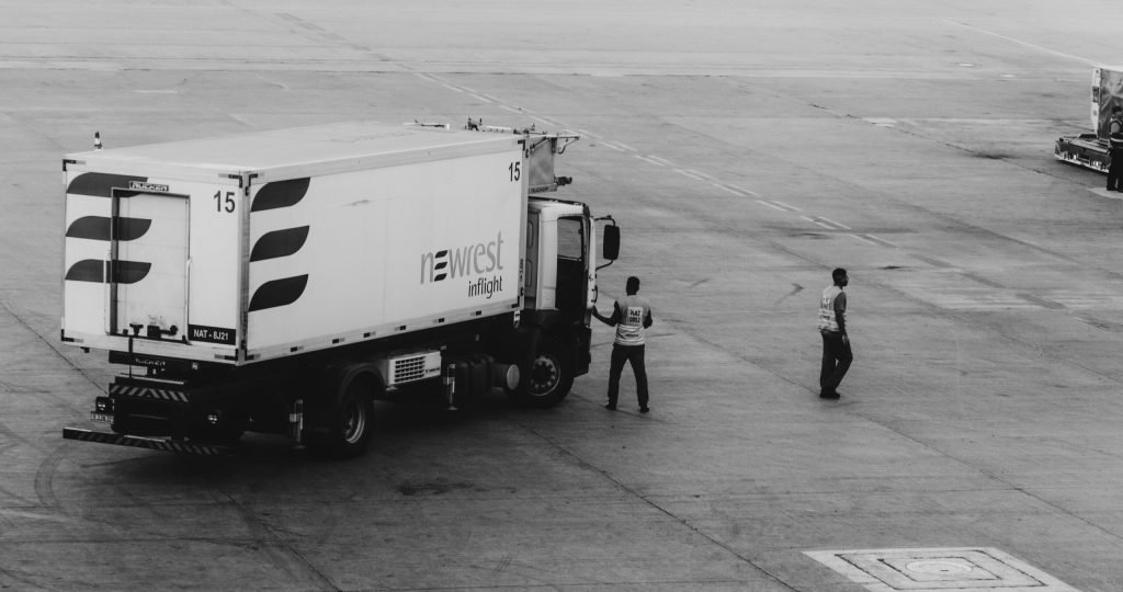 Black and white photo of a catering truck with crew on an airport tarmac.