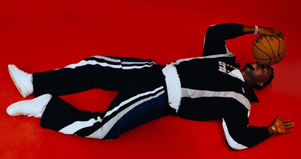 Stylish man in streetwear lies on red floor holding a basketball, exuding urban cool.