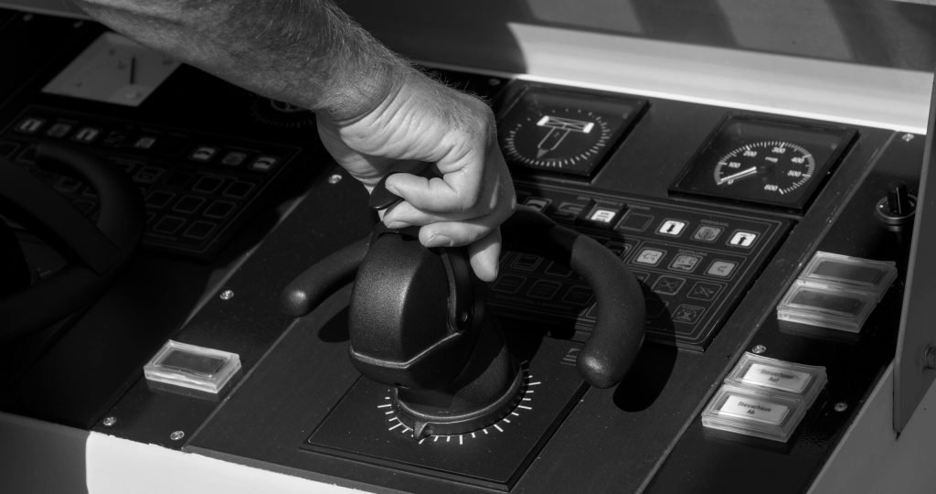 Black and white image of a person's hand adjusting a throttle lever on a boat control panel.