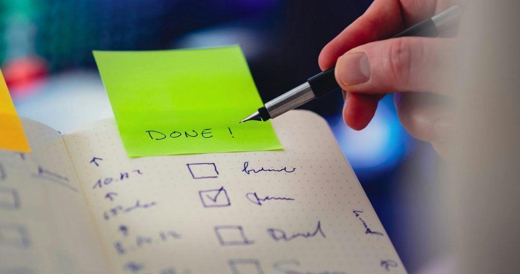 Close-up of a checklist and pen with brightly colored sticky note that says 'DONE!' indicating task completion.
