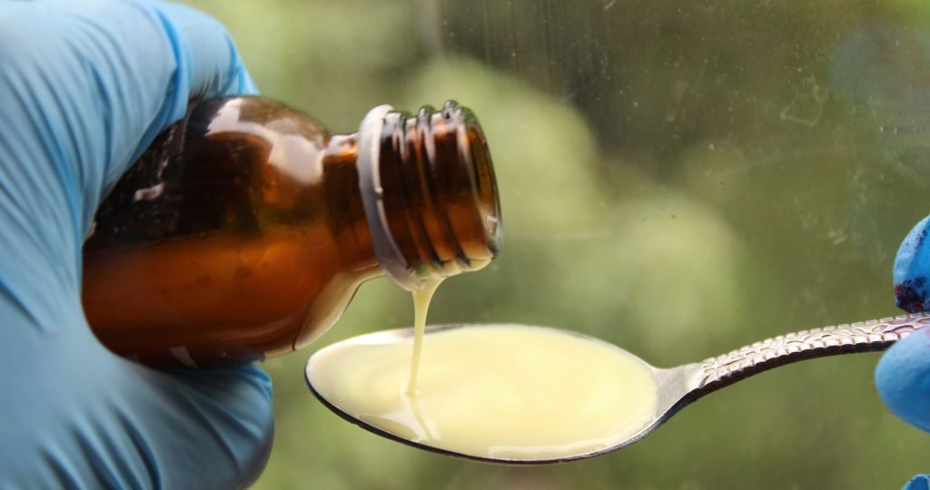 Close-up of liquid medicine being poured into a spoon, captured with gloves for medical use.