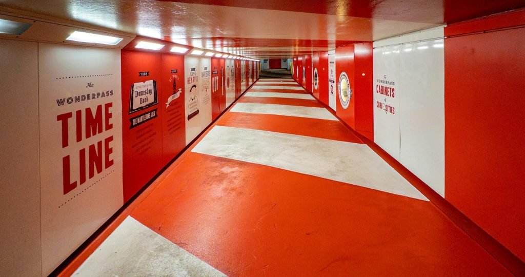 Brightly lit red and white tunnel in London showcasing vibrant artwork and signs.