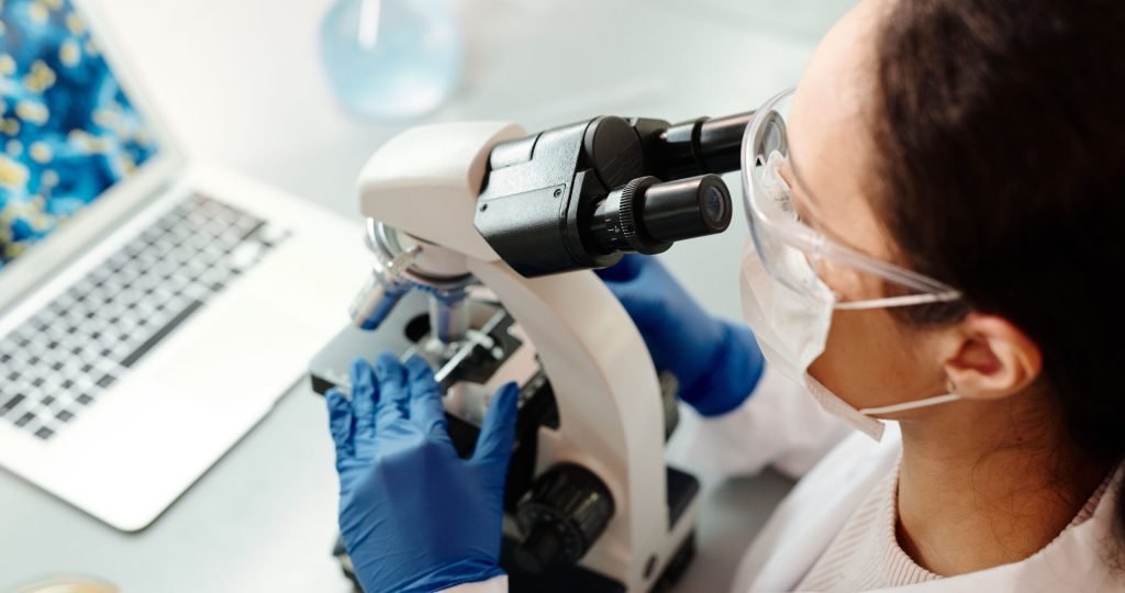 Scientist in protective gear examining samples with microscope in laboratory setting.