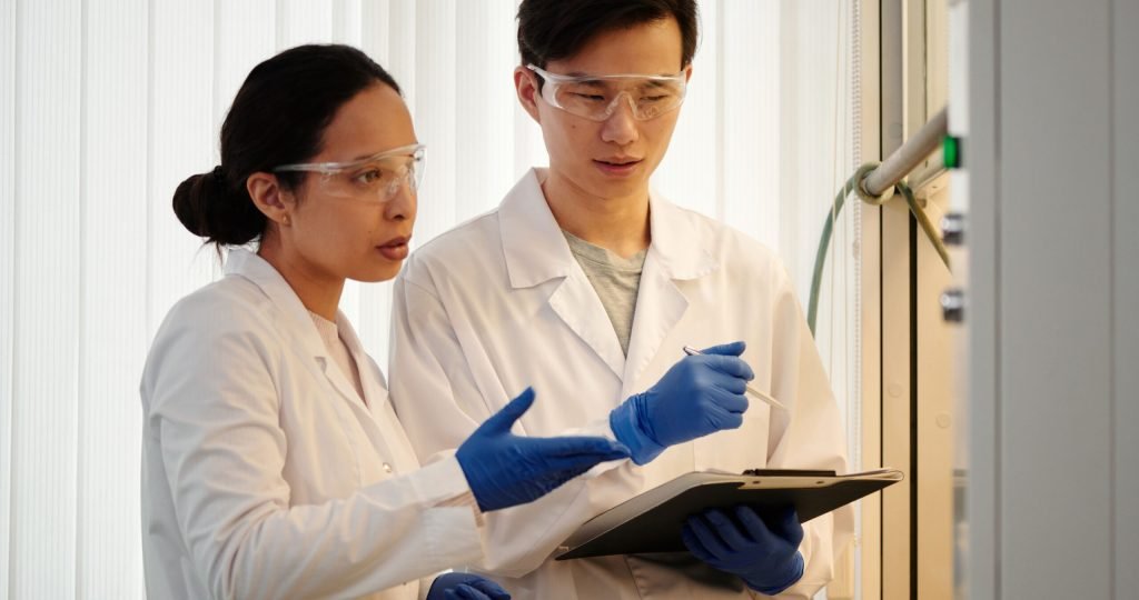 Researchers discussing data in a laboratory setting, wearing safety gear and blue gloves.