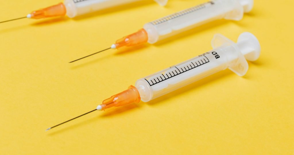 Plastic empty medical syringe injectors with orange needle hubs and without protective cover placed on bright yellow surface