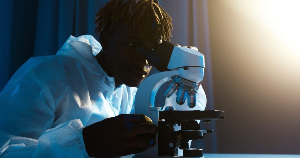 A scientist in protective clothing uses a microscope for research in a laboratory setting.
