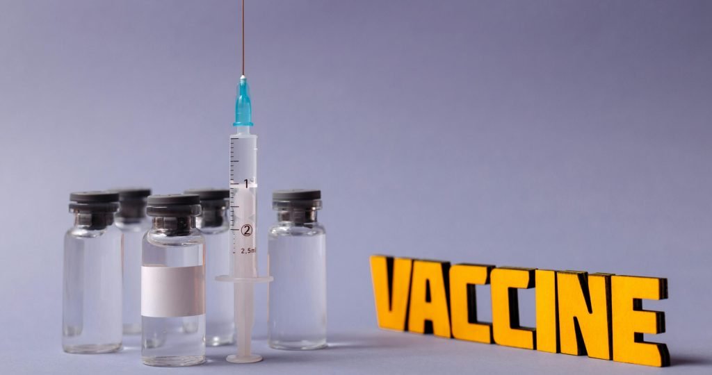 Syringe and vaccine vials with 'vaccine' text on a gray background, representing vaccination efforts.