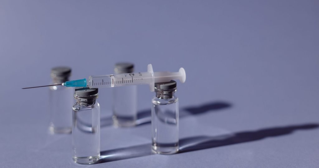 A syringe balanced on vaccine vials with a purple backdrop, representing medical treatment.