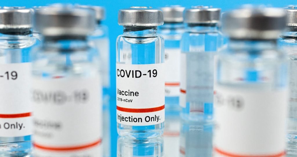 Close-up of COVID-19 vaccine vials on a reflective surface against a blue background.