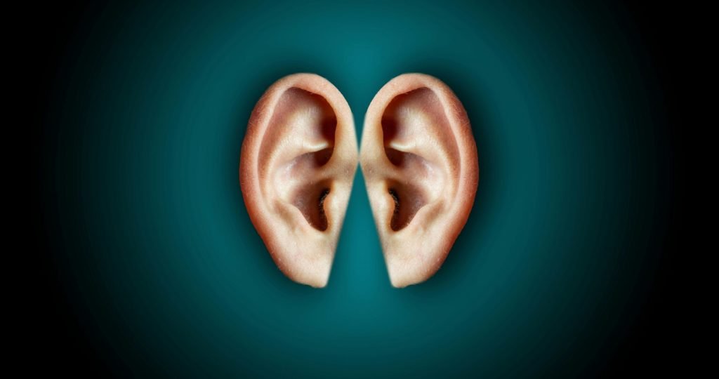Creative unusual composition of human ears arranged close on center of dark blue background