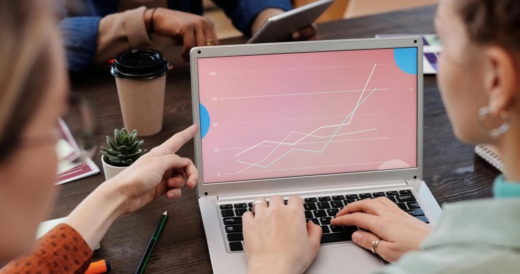 Office workers collaboratively reviewing data trends on a laptop during a meeting.