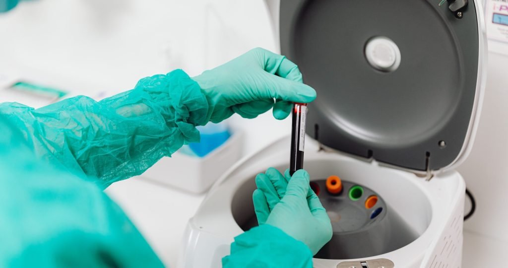 Lab technician operates a centrifuge machine, handling tubes with gloves.
