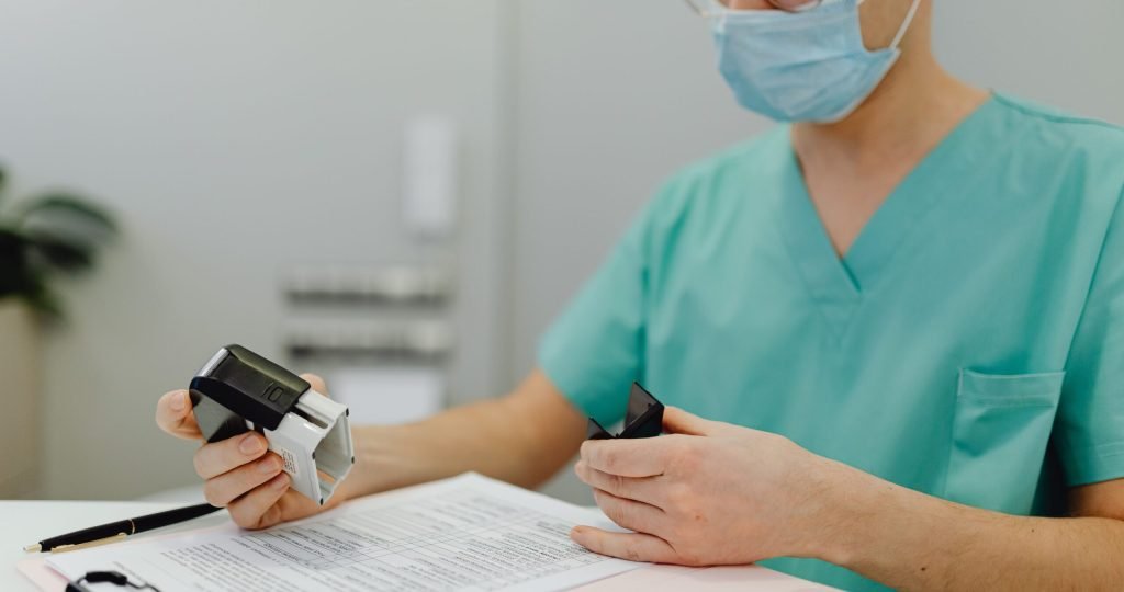 Healthcare worker in scrubs reviewing patient files with a stamp and clipboard.