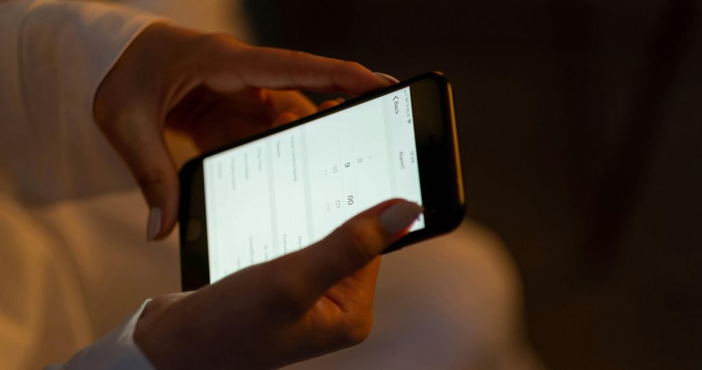 Close-up of hands setting an alarm on a smartphone, depicting night usage and technology interaction.